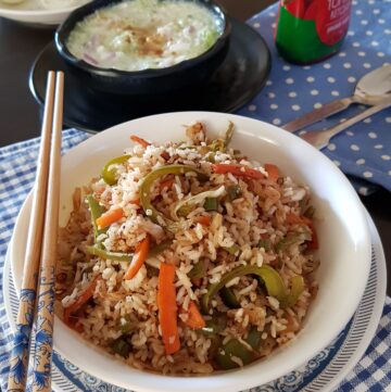 vegetable fried rice in a white bowl with two chopsticks.