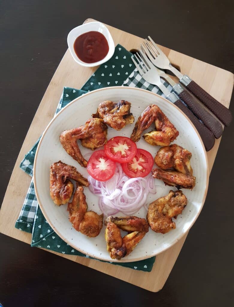 chicken wings served on a white round plate and garnished with onion and tomatoes.
