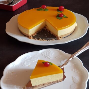 no bake mango cheesecake is cut and a slice is served on a white plate