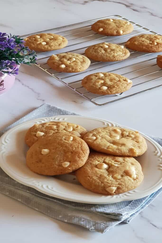 soft, chewy white chocolate chip cookies on a cooling rack and a plate.