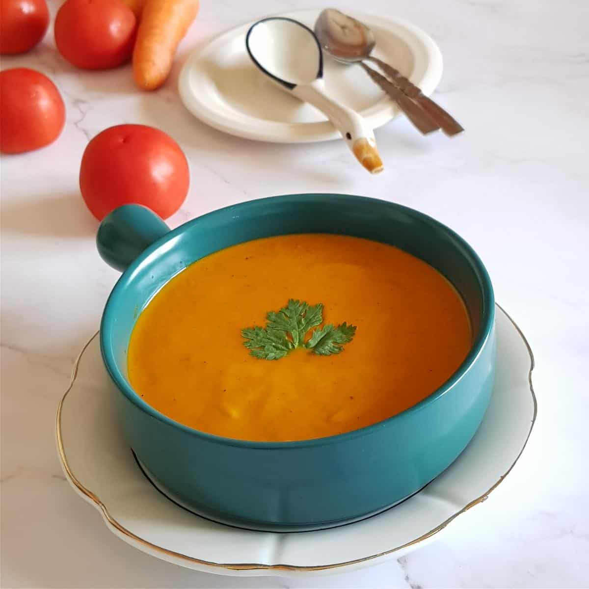 Tomato carrot soup without cream served in a bowl with fresh coriander garnish and a creamy smooth texture.