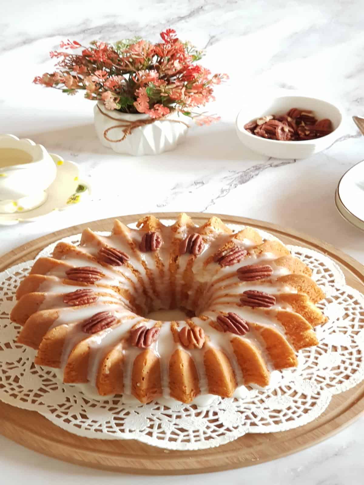 Banana cake with vanilla glaze and pecans served on a wooden board.